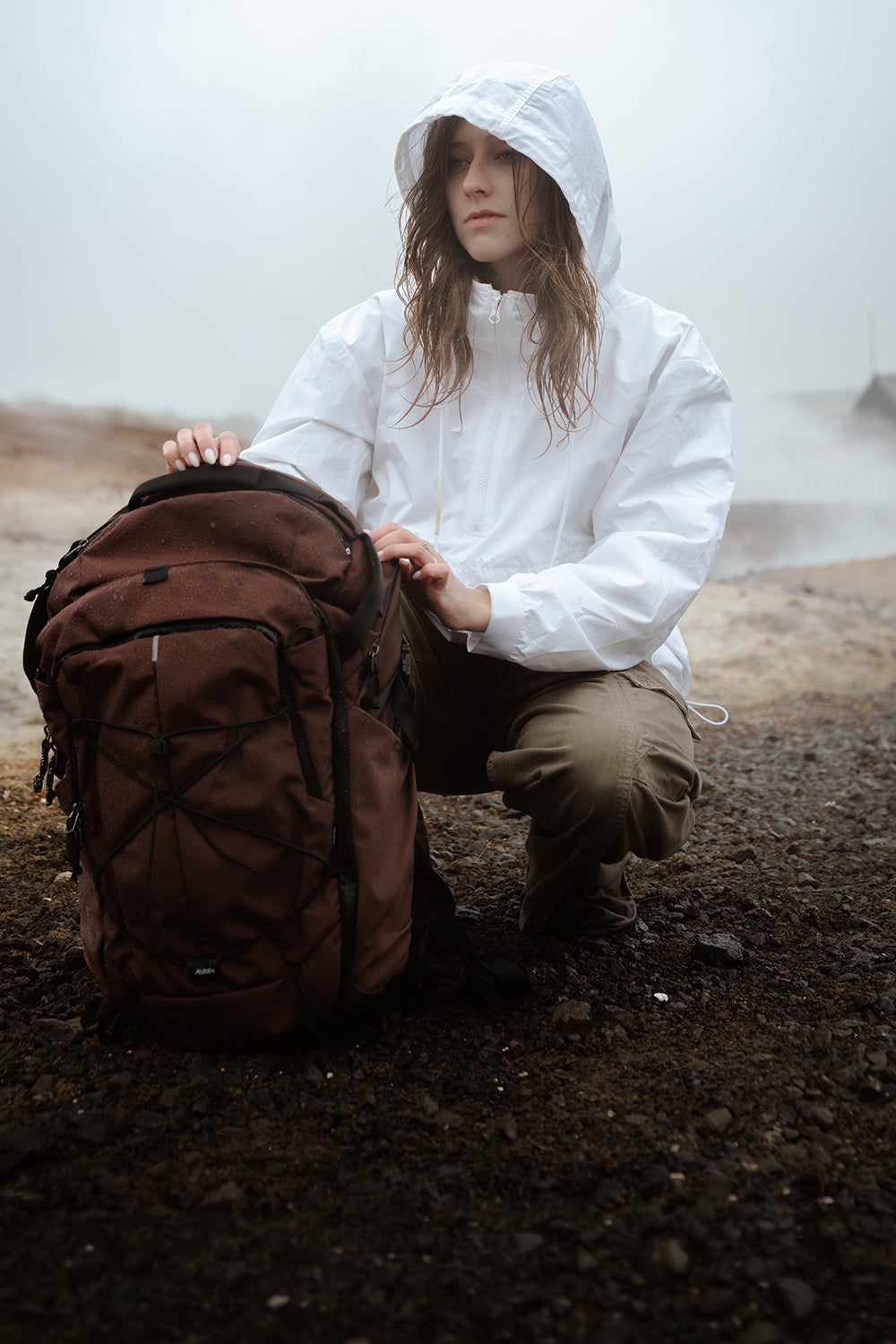person in white jacket in moody setting with garnet backpack