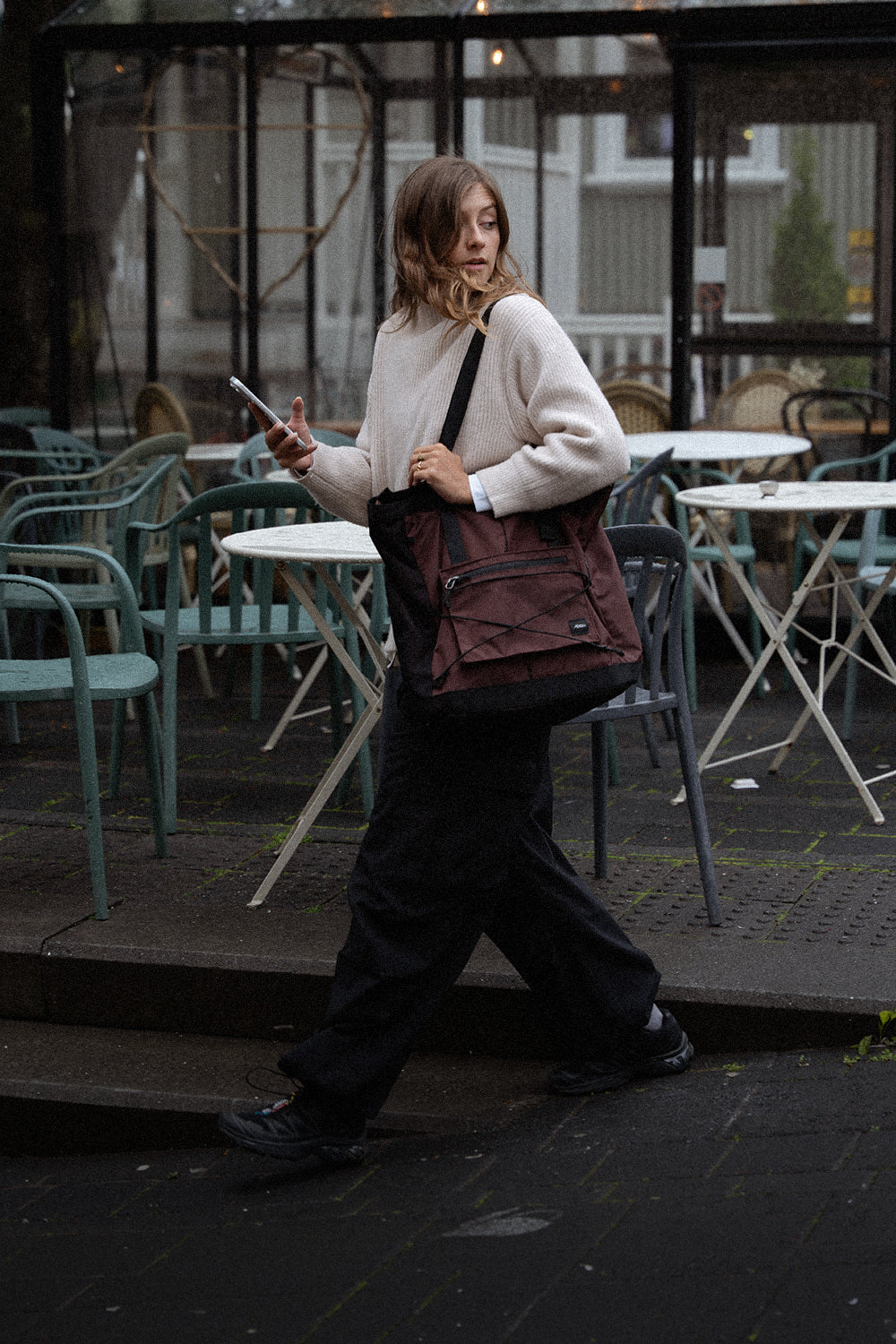 person leaving cafe with cell phone and garnet tote