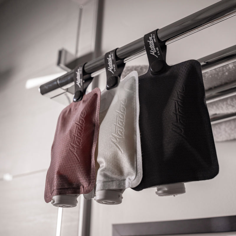 Garnet, Arctic White, and Charcoal Flatpak toiletry bottle hanging from chrome bathroom rack