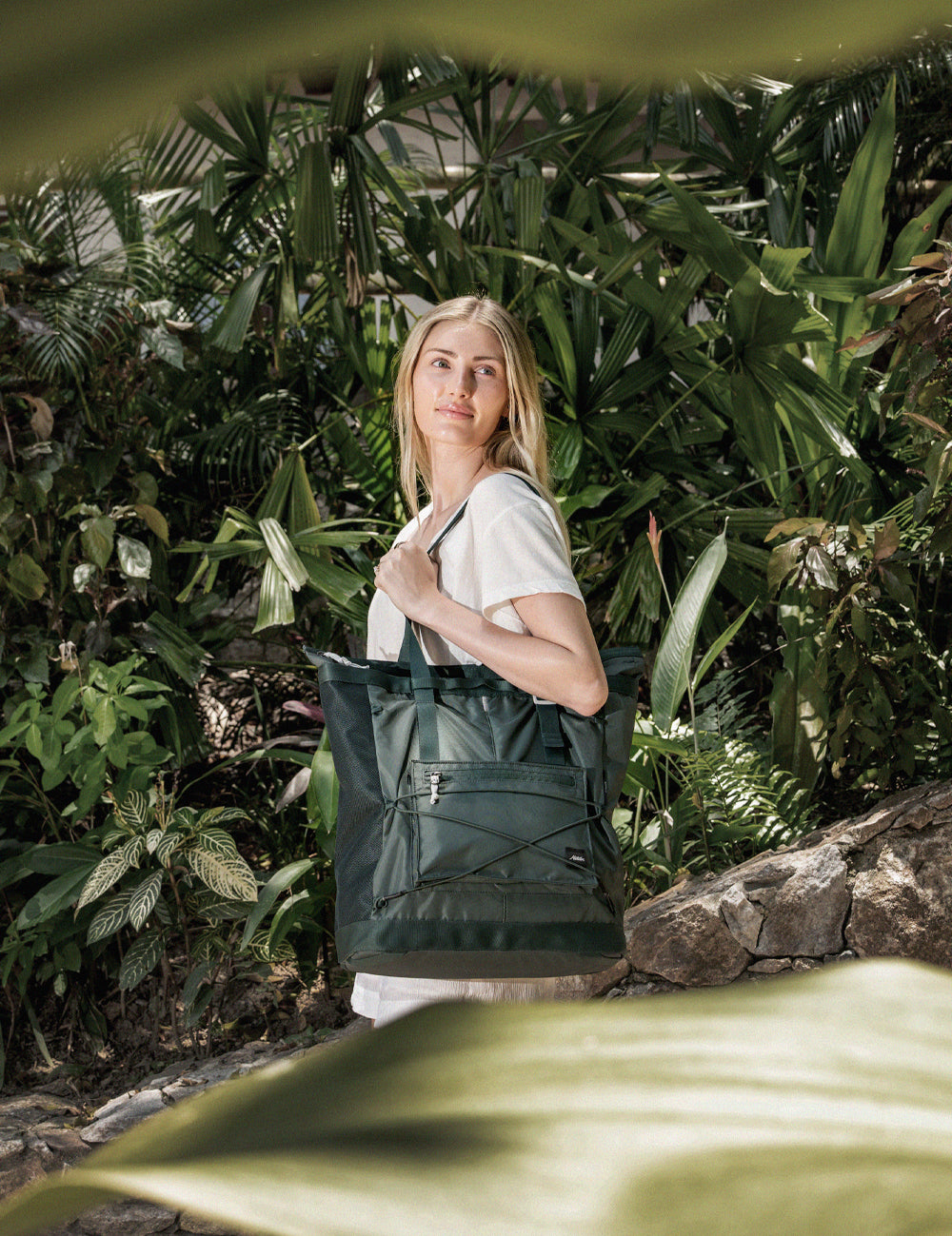 Person among tropical leaves holding juniper tote pack