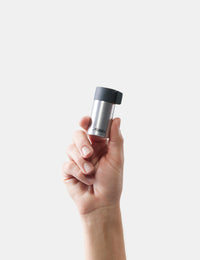 Hand holding a silver and black container against a white background