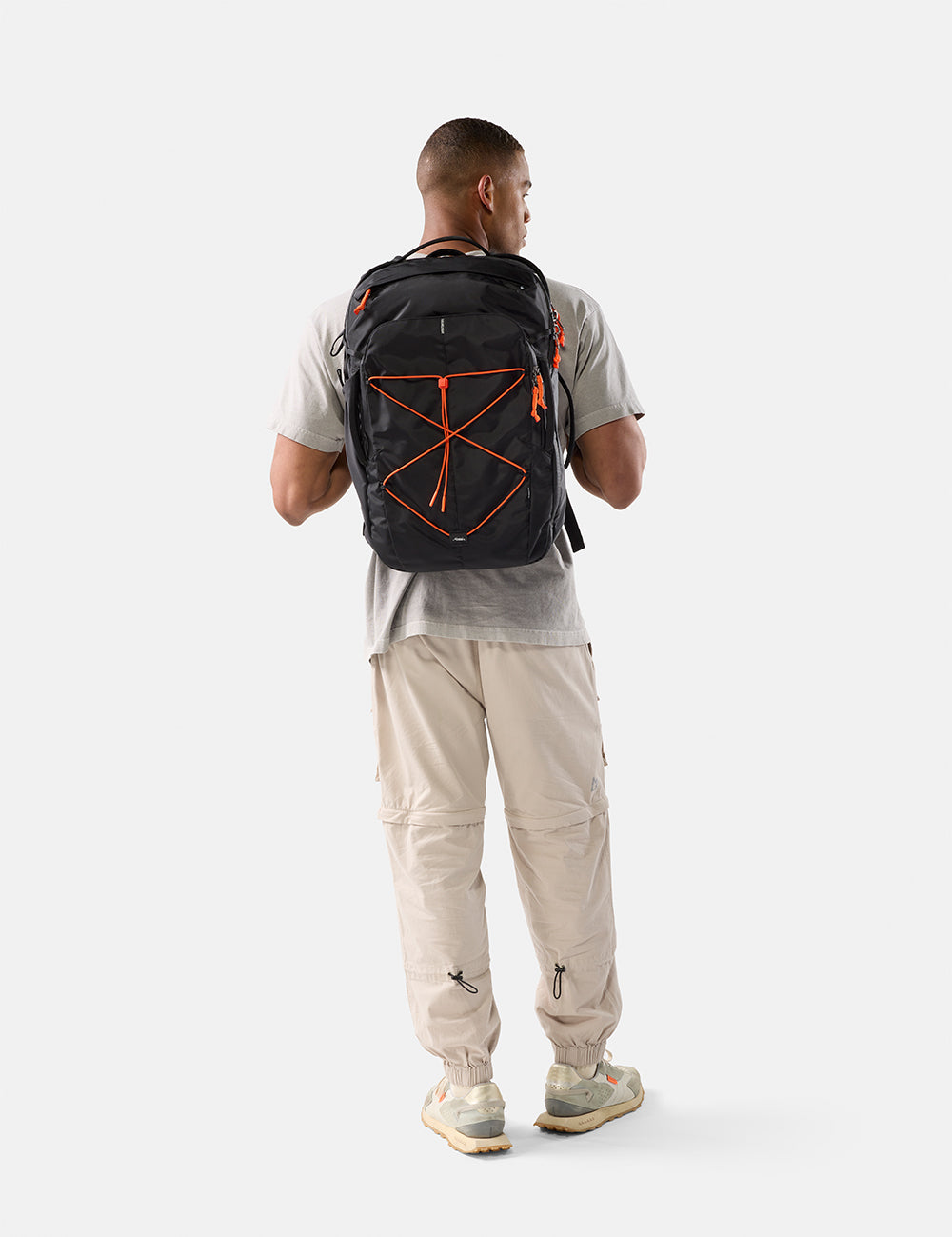 Man wearing a black backpack with orange accents on a white background