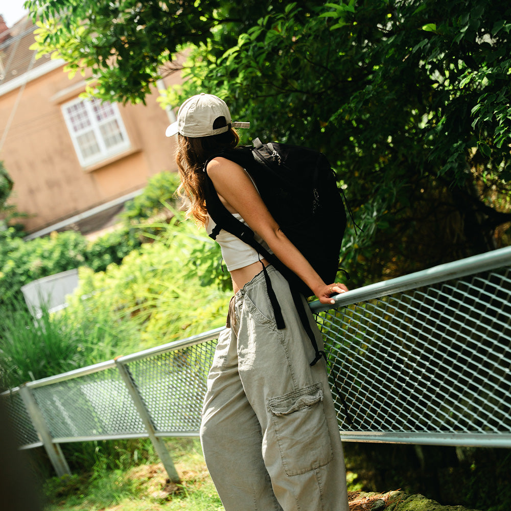 person leaning in tree filled park wearing black backpack
