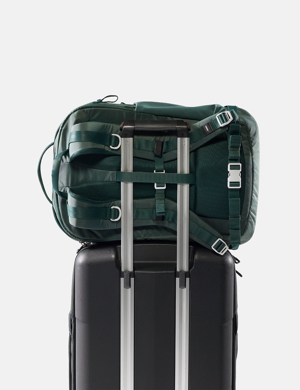 Green backpack on top of a black suitcase with silver handles on a white background