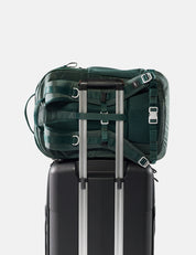 Green backpack on top of a black suitcase with silver handles on a white background