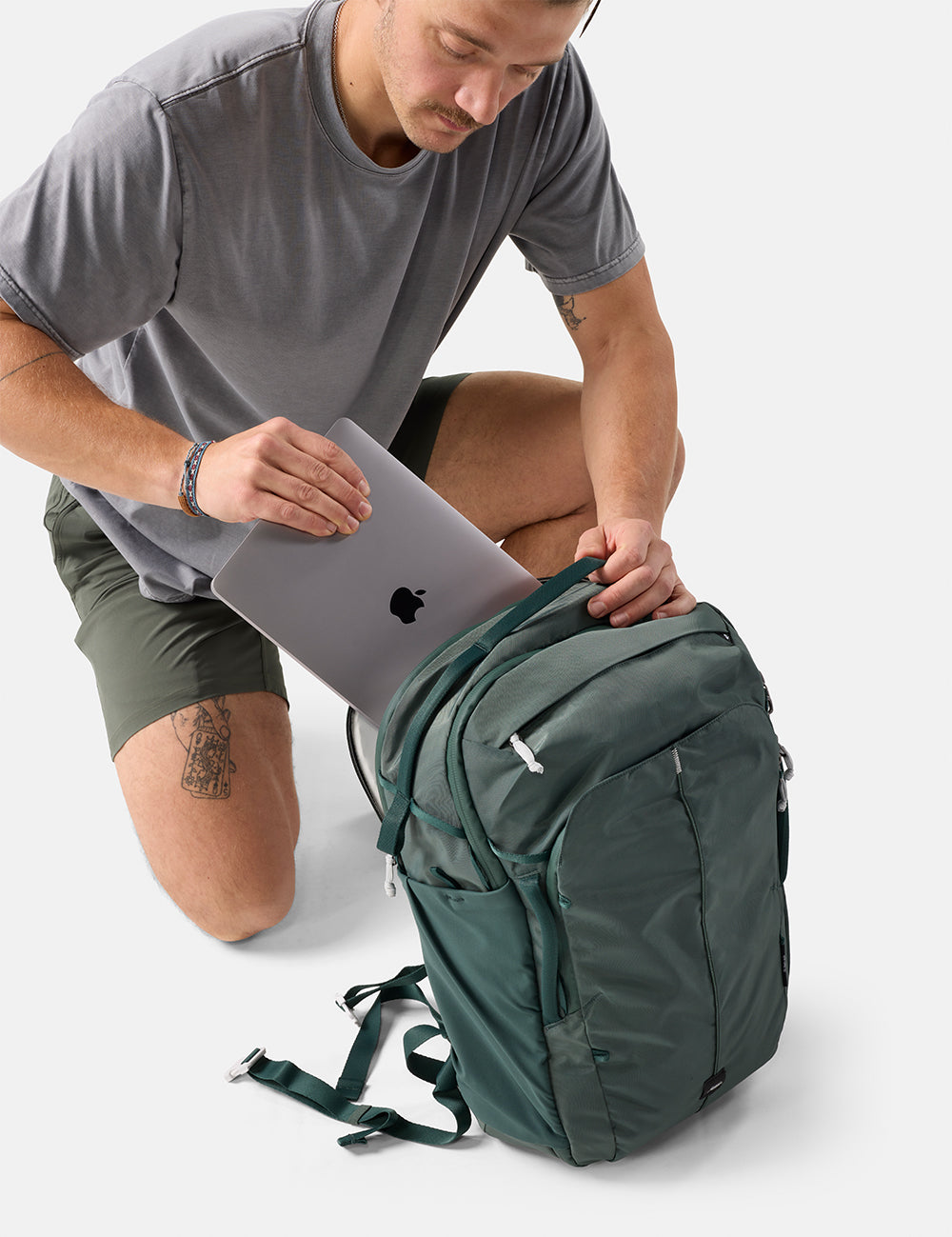 Man placing a laptop into a green backpack on a white background