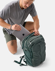 Man placing a laptop into a green backpack on a white background
