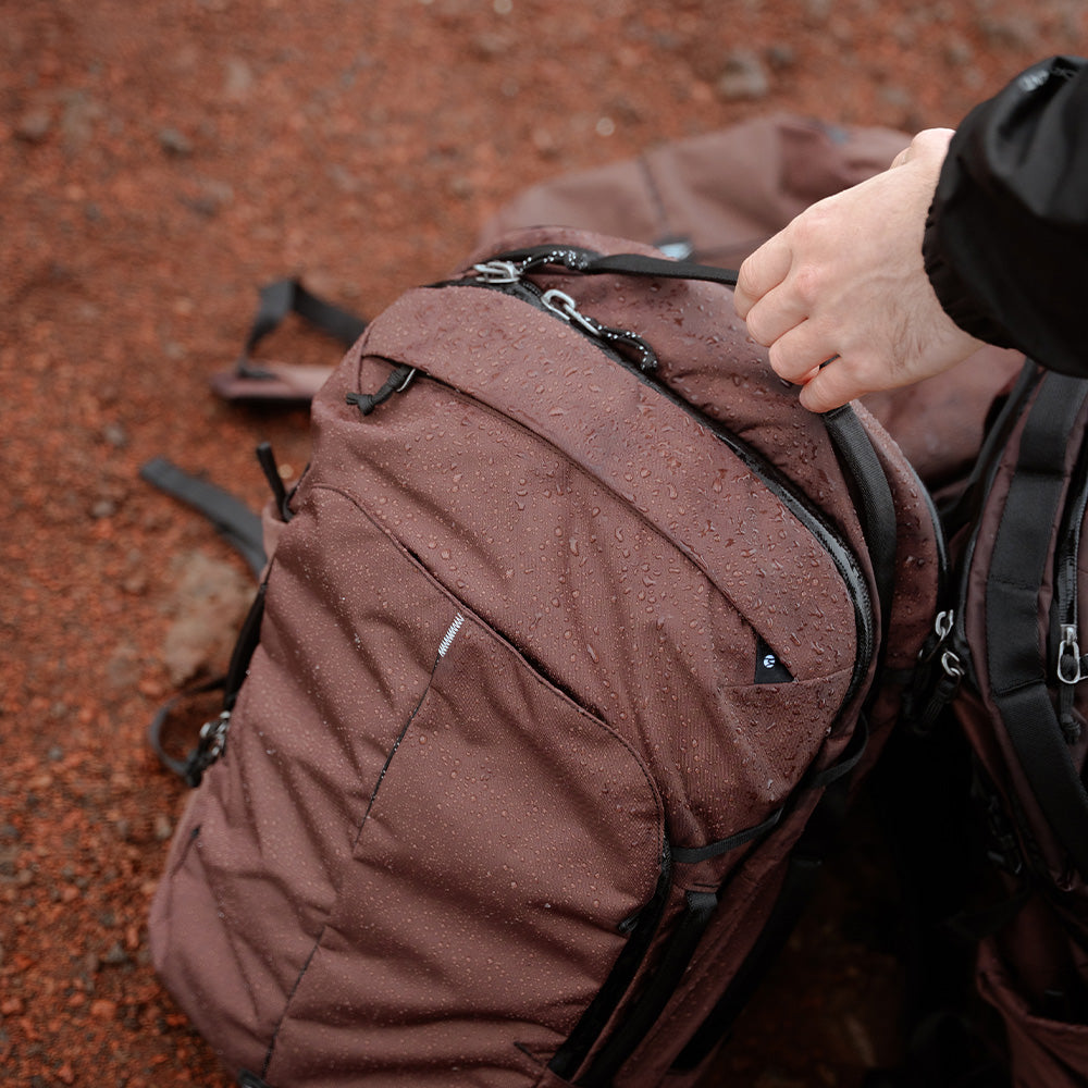 hand grabbing garnet backpack covered in water drops