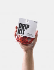 Hand holding a 'Drip Kit' packaging with orange components against a white background