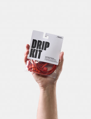Hand holding a 'Drip Kit' packaging with orange components against a white background