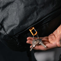man pulling keys and orange carabiner out of black backpack