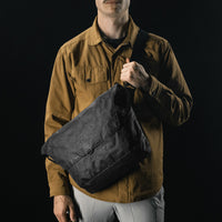 man on black studio background wearing black messenger bag across his front