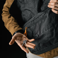 man holding keys attached to orange carabiner attachment from inside black messenger