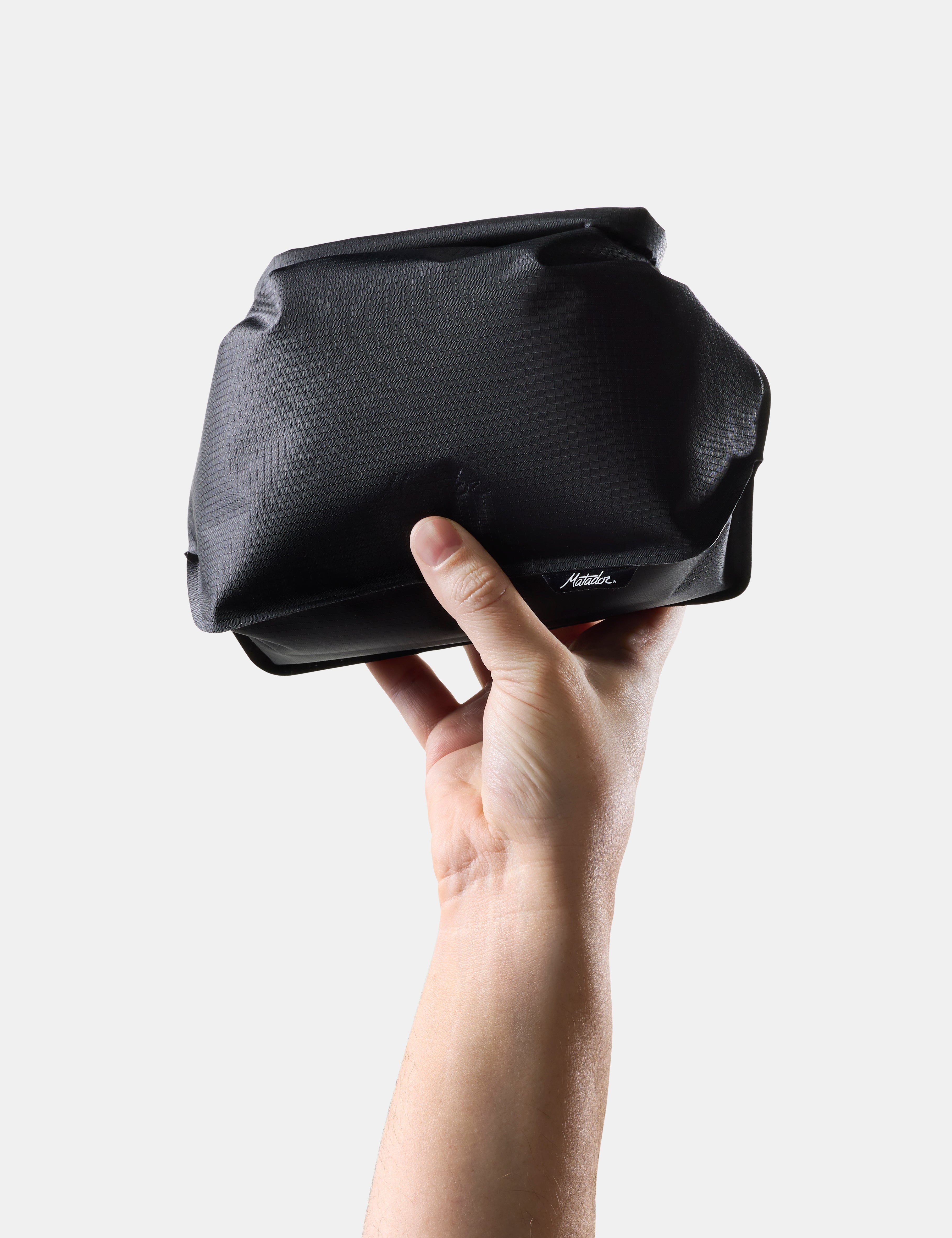 Hand holding a Black toiletry case on a light gray background
