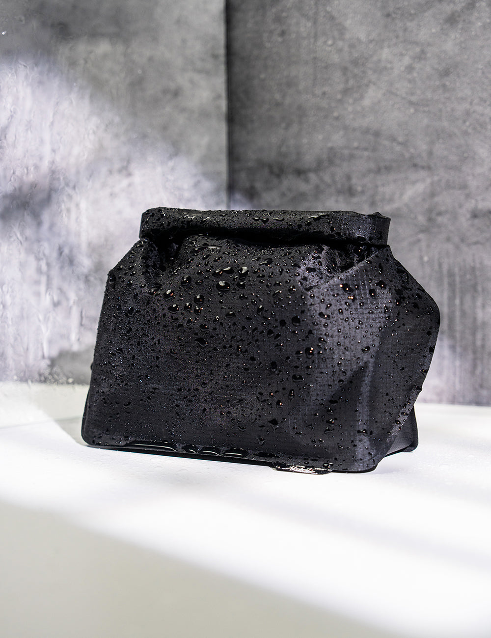 Water droplet covered black toiletry case in concrete bathroom