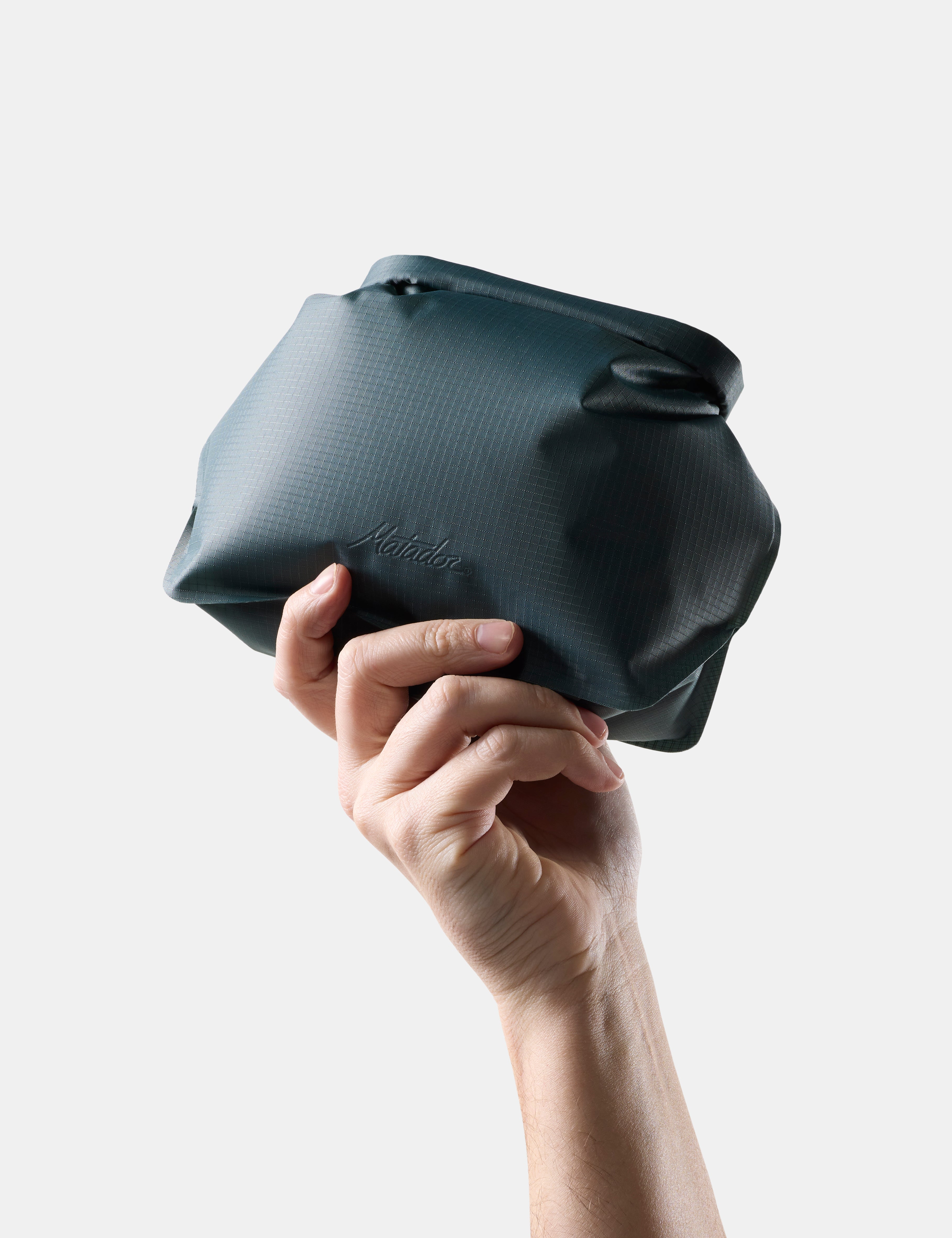 Hand holding a Blue-green toiletry bag against a light gray background