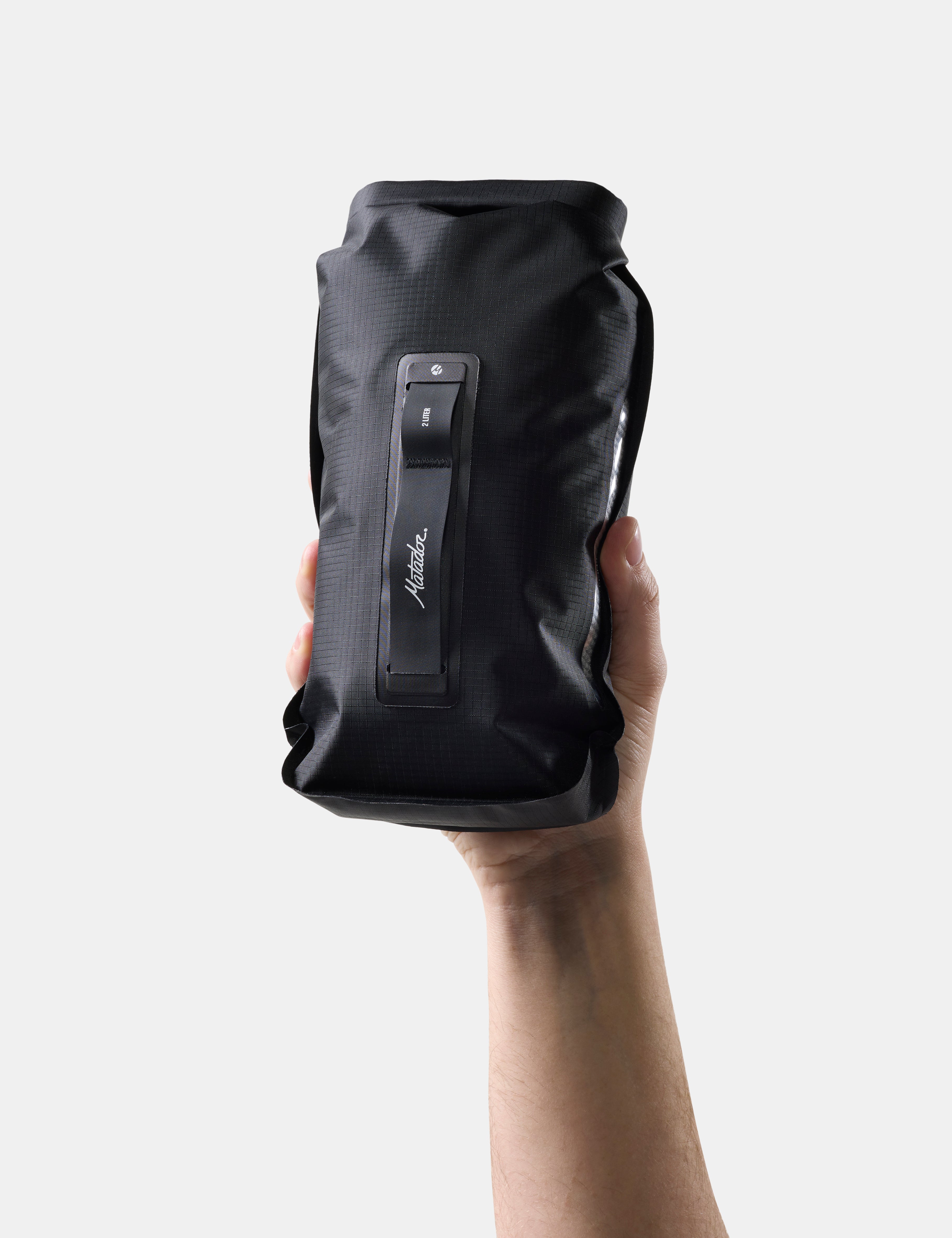 Black dry bag held by a hand on a white background