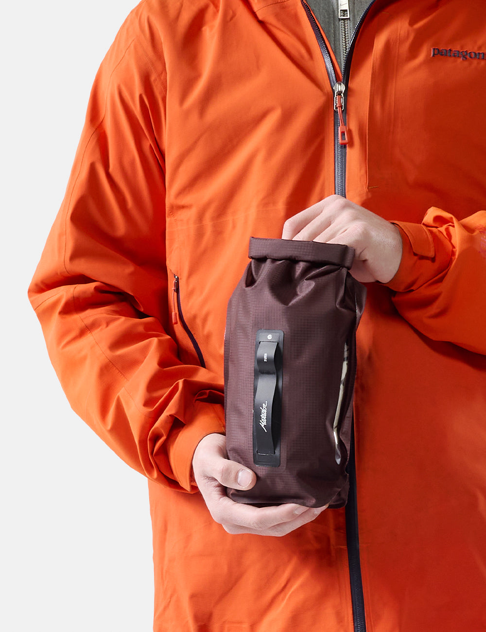 Person wearing an orange jacket holding a garnet dry bag  on a white background
