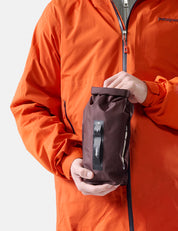 Person wearing an orange jacket holding a garnet dry bag  on a white background