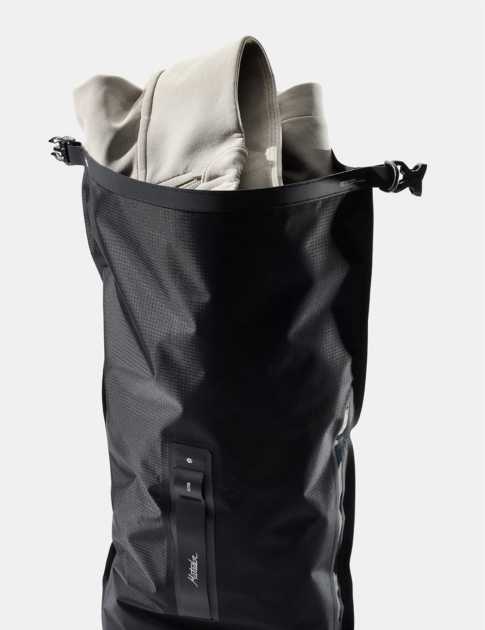 Black dry bag containing a light-colored jacket on a white background