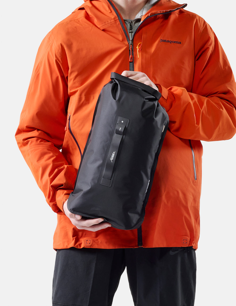 Person wearing an orange jacket holding a black dry bag