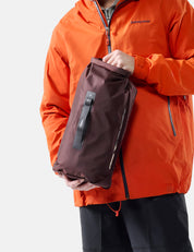 Person wearing an orange jacket holding a garnet dry bag against a white background
