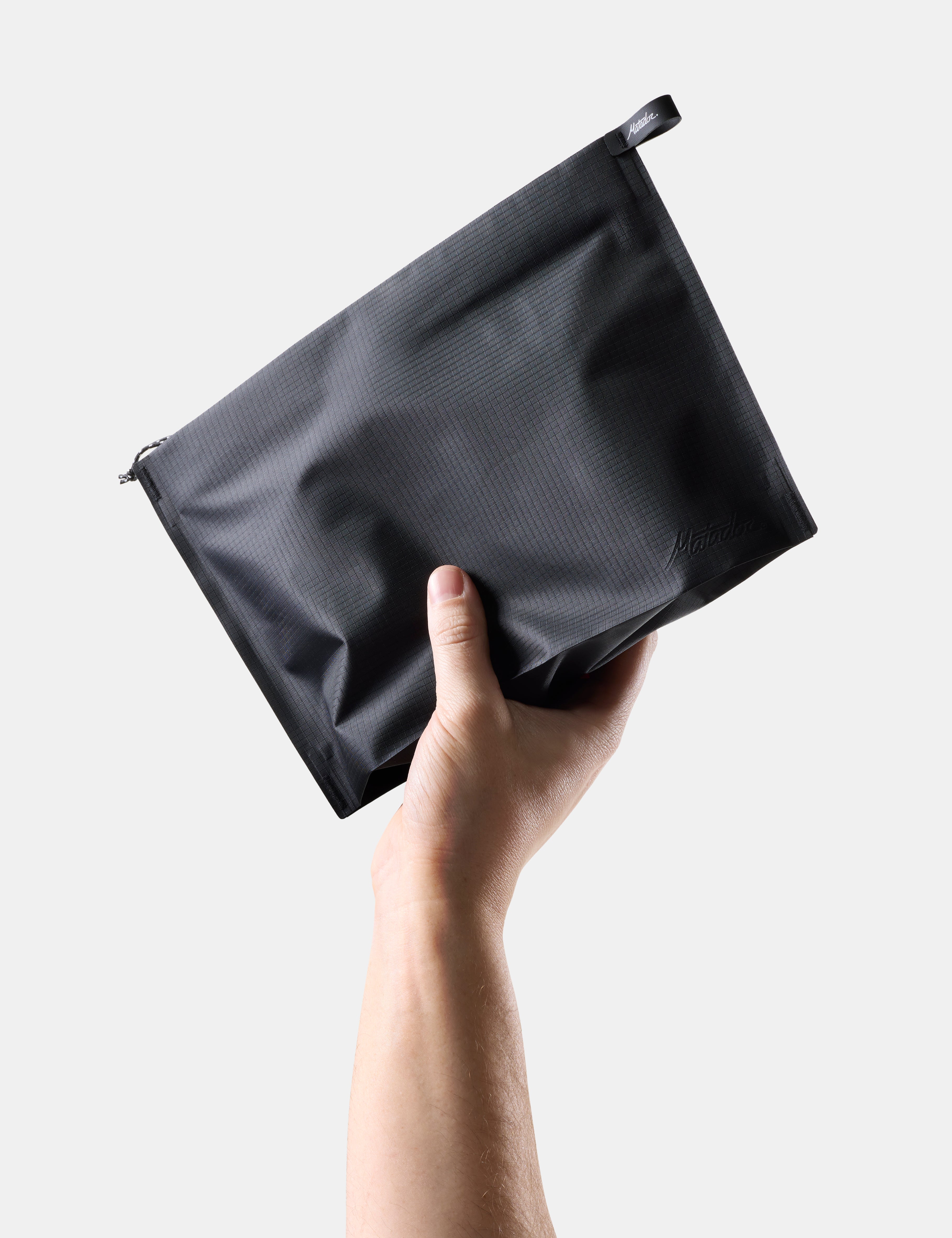 Hand holding a Black zippered toiletry case against a light gray background