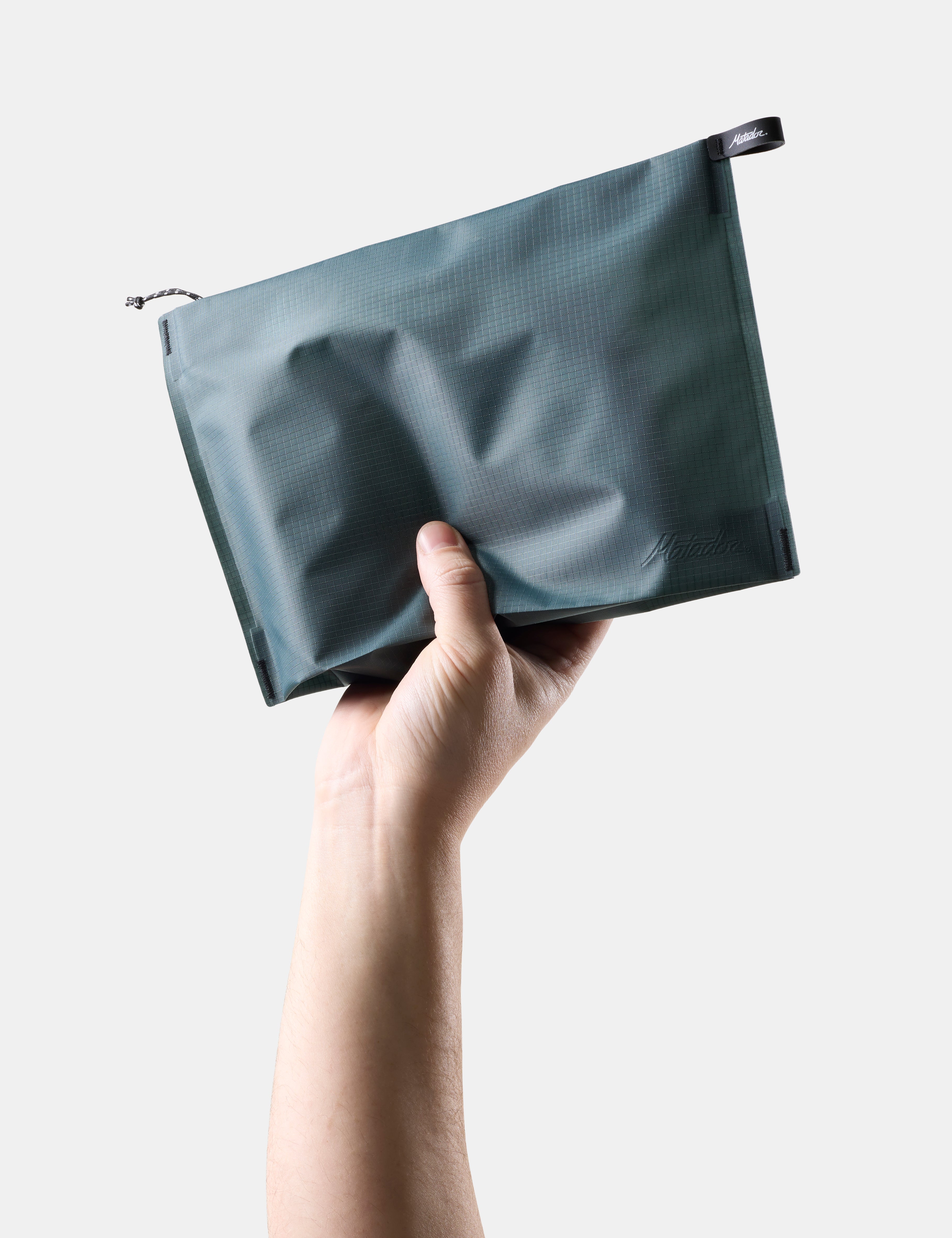 Hand holding a Blue-green zipper toiletry case against a light background