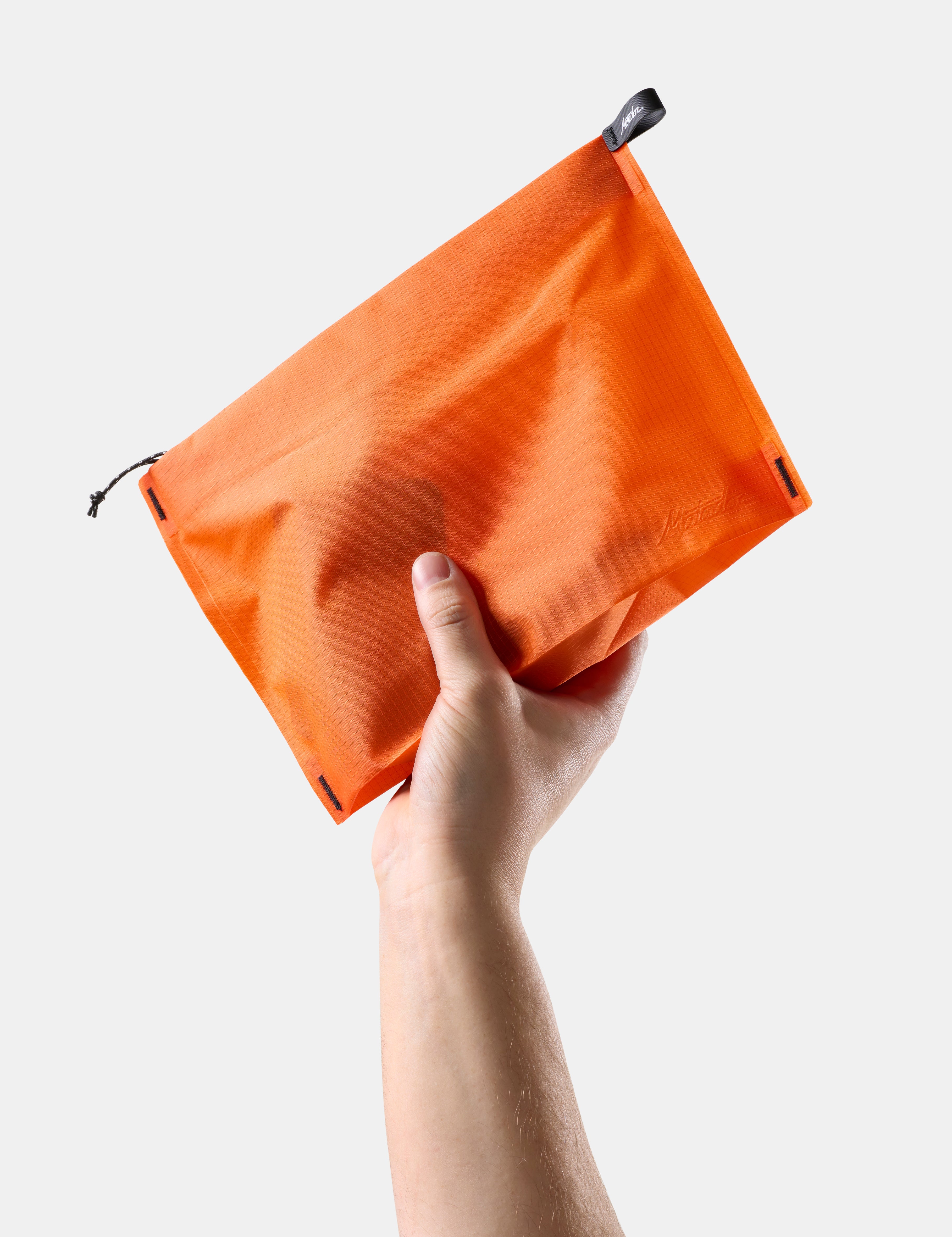 Hand holding an Orange zipper toiletry case against a light gray background