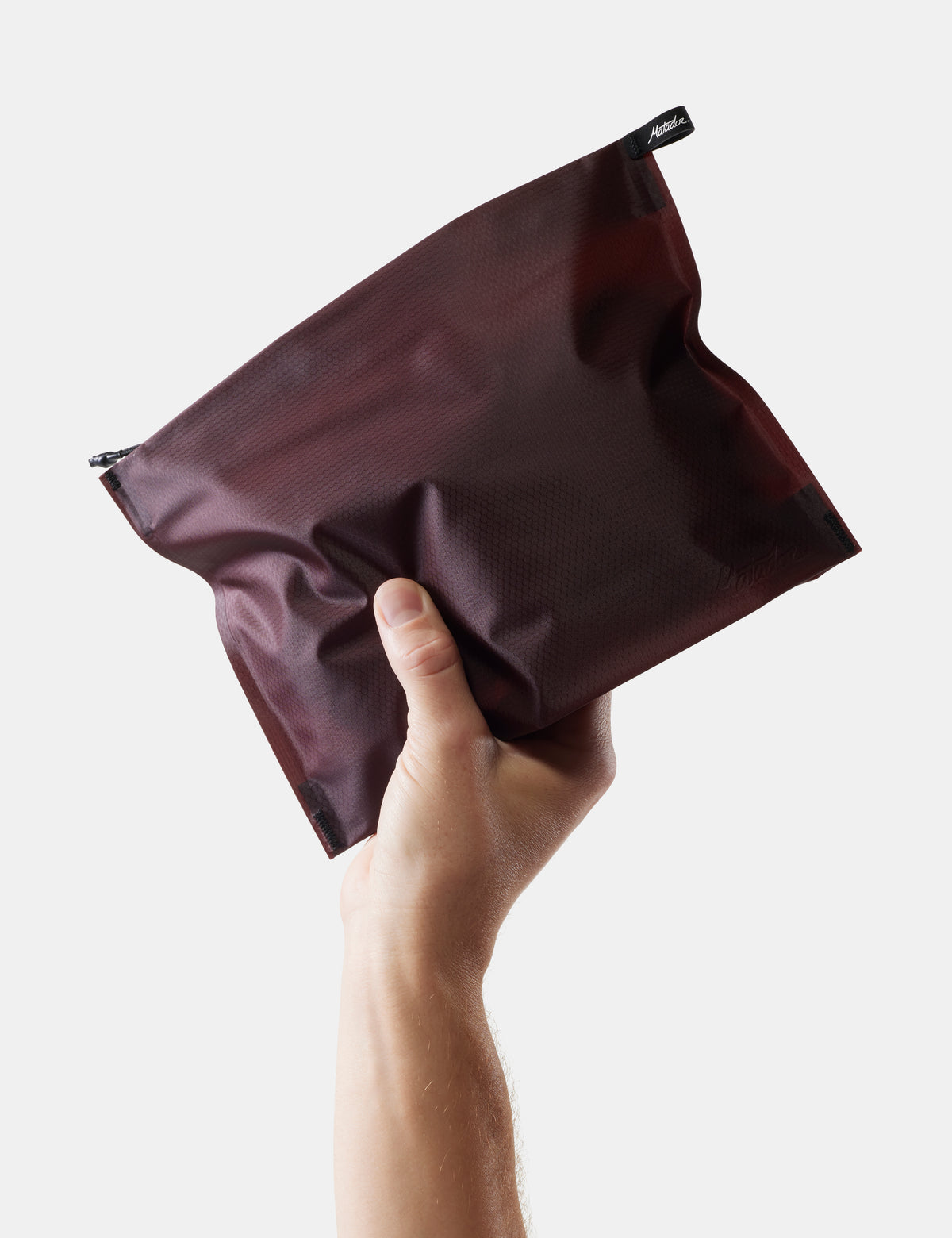 Hand holding a garnet toiletry case against a light gray background