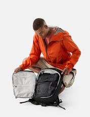 Person in an orange jacket opening a black backpack on a white background