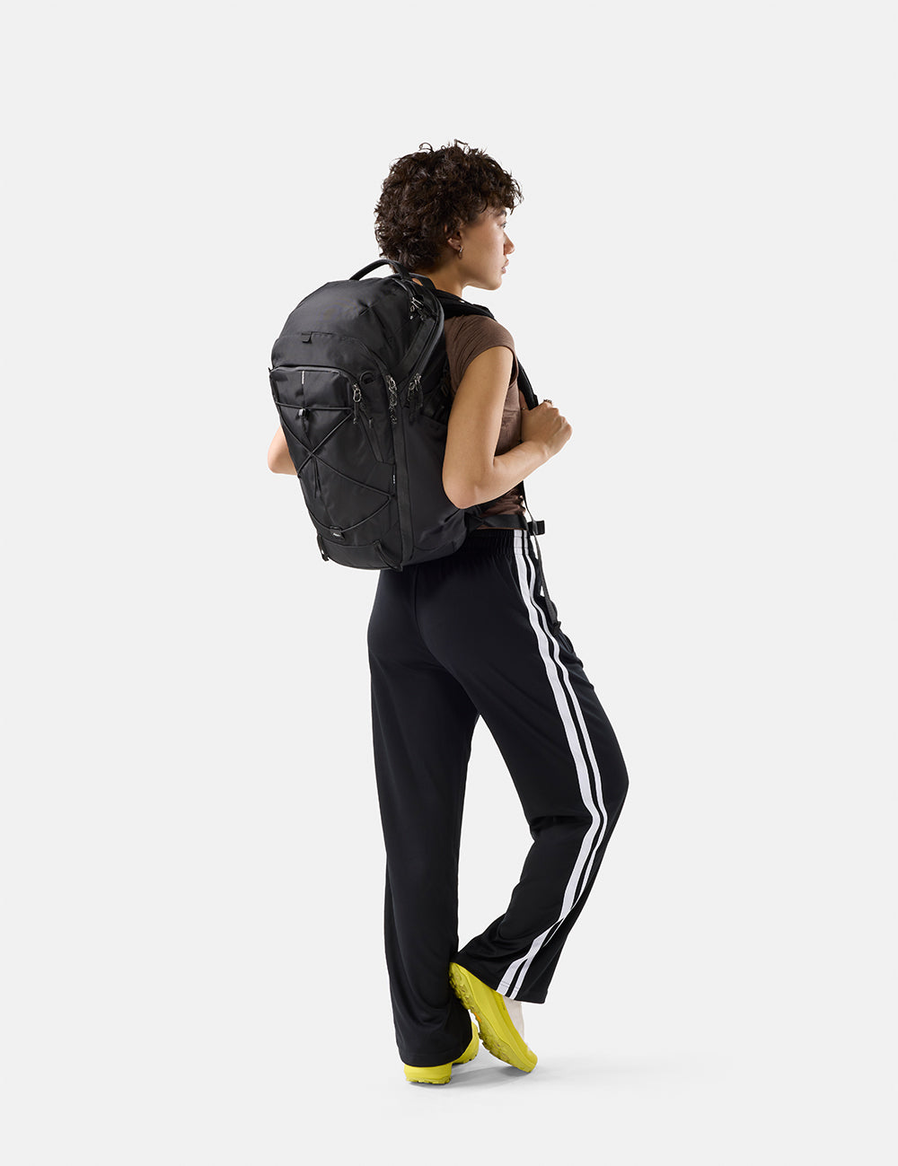 Person wearing a black backpack and black pants with white stripes on a white background