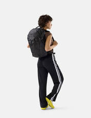 Person wearing a black backpack and black pants with white stripes on a white background