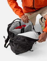 Person opening a black backpack with a white interior on a light gray background