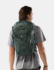 A man wearing a dark green technical backpack, viewed from behind to show the fit and design, against a light gray studio background.