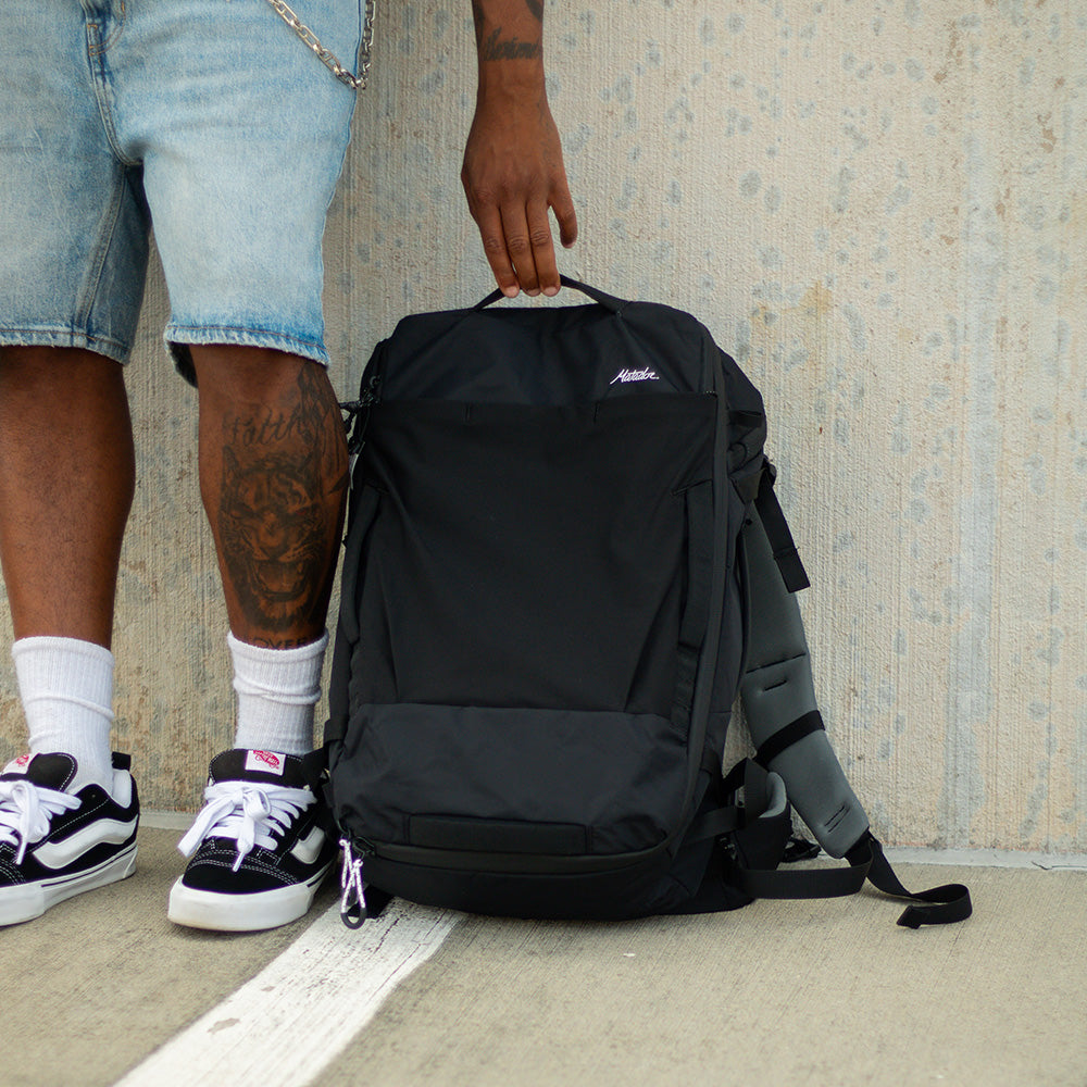 man grabbing black backpack laying against concrete wall