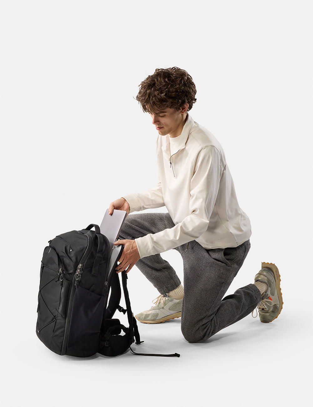 Man sitting on the floor with a black backpack and laptop on a white background
