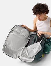 Person organizing a green backpack with multiple compartments on a white background