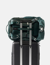 Green backpack on top of a black suitcase with a white background