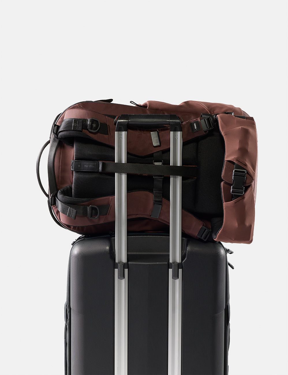 garnet backpack on top of a black suitcase with silver handle on a light gray background