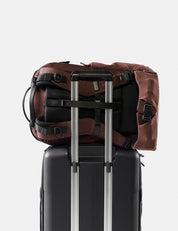 garnet backpack on top of a black suitcase with silver handle on a light gray background