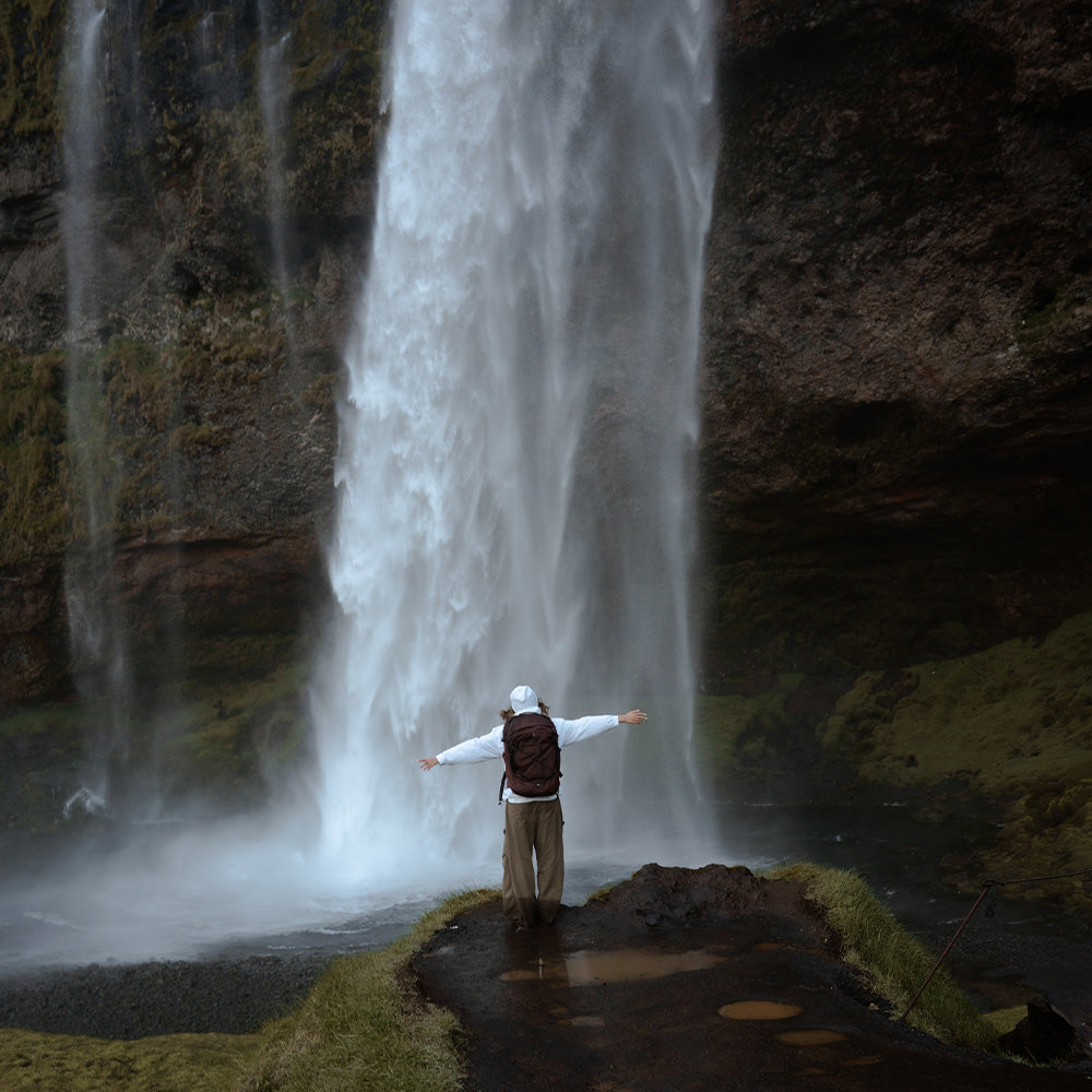 person in white jacket in front of iceland waterfall