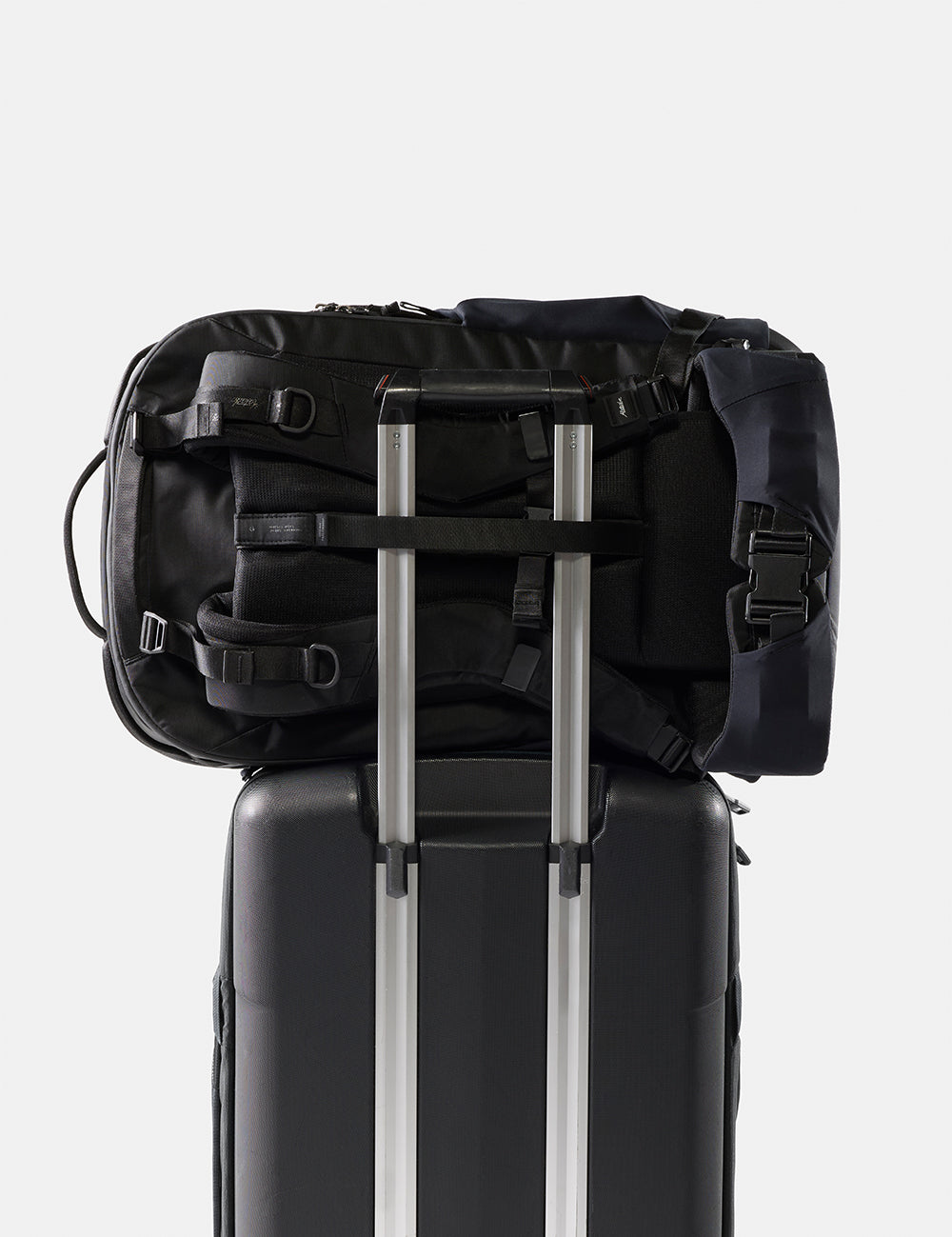Black backpack on top of a suitcase with a white background