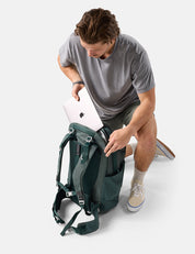 Man placing a laptop into a green backpack on a white background