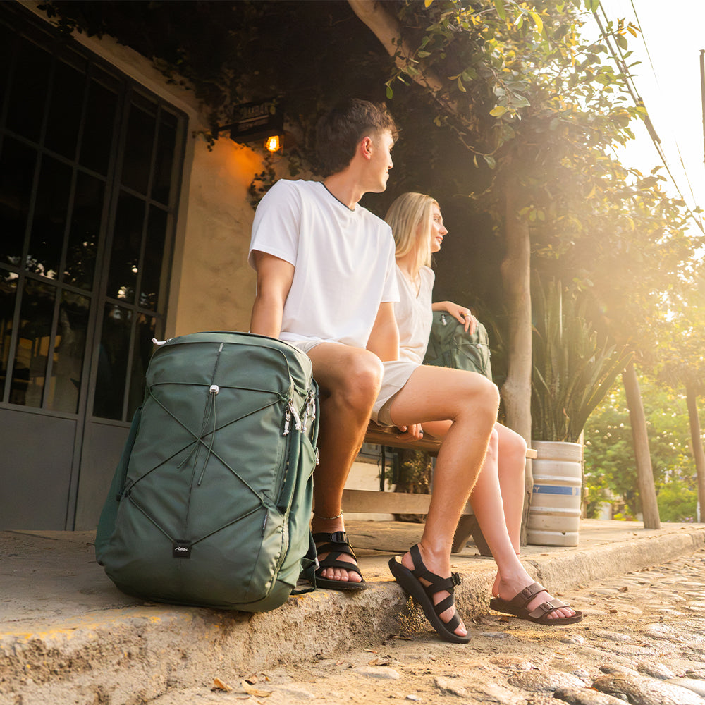 people sitting on sunny bench on cobblestone street with juniper bags