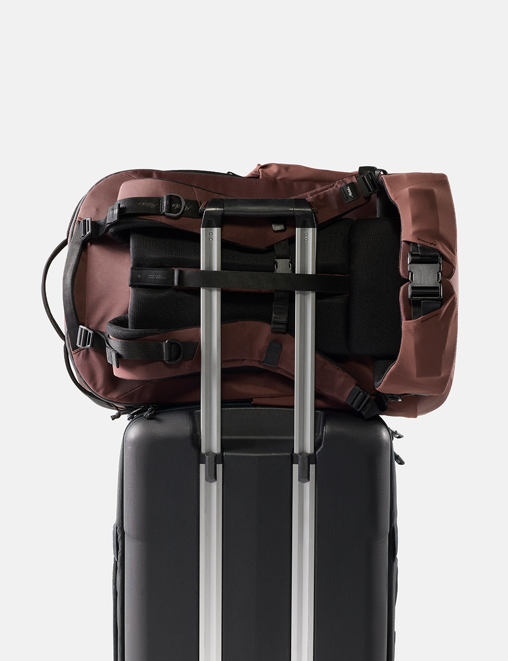 garnet backpack on top of a black suitcase with silver handle on a white background