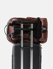 garnet backpack on top of a black suitcase with silver handle on a white background