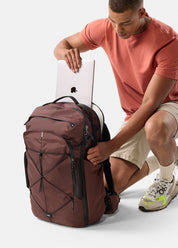 Man placing a laptop into a garnet backpack on a white background