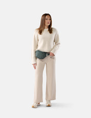 Woman wearing a cream sweater and beige pants with a green fanny pack on a white background