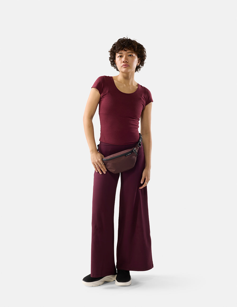 Woman wearing a maroon outfit with a belt bag on a white background